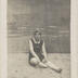 "Denise" femme en maillot de bain, assise sur du sable devant un décor peint
