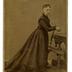 portrait en pied d'une jeune femme en studio, accoudée à une chaise  devant une table d'une table