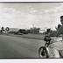 de la série "Isla" "Andris" portrait en demi hauteur et de profil d'un homme sur sa moto circulant sur une route bordée par un panneau de propagande communiste avec un portrait de Che Guevara