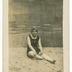 "Denise" femme en maillot de bain, assise sur du sable devant un décor peint